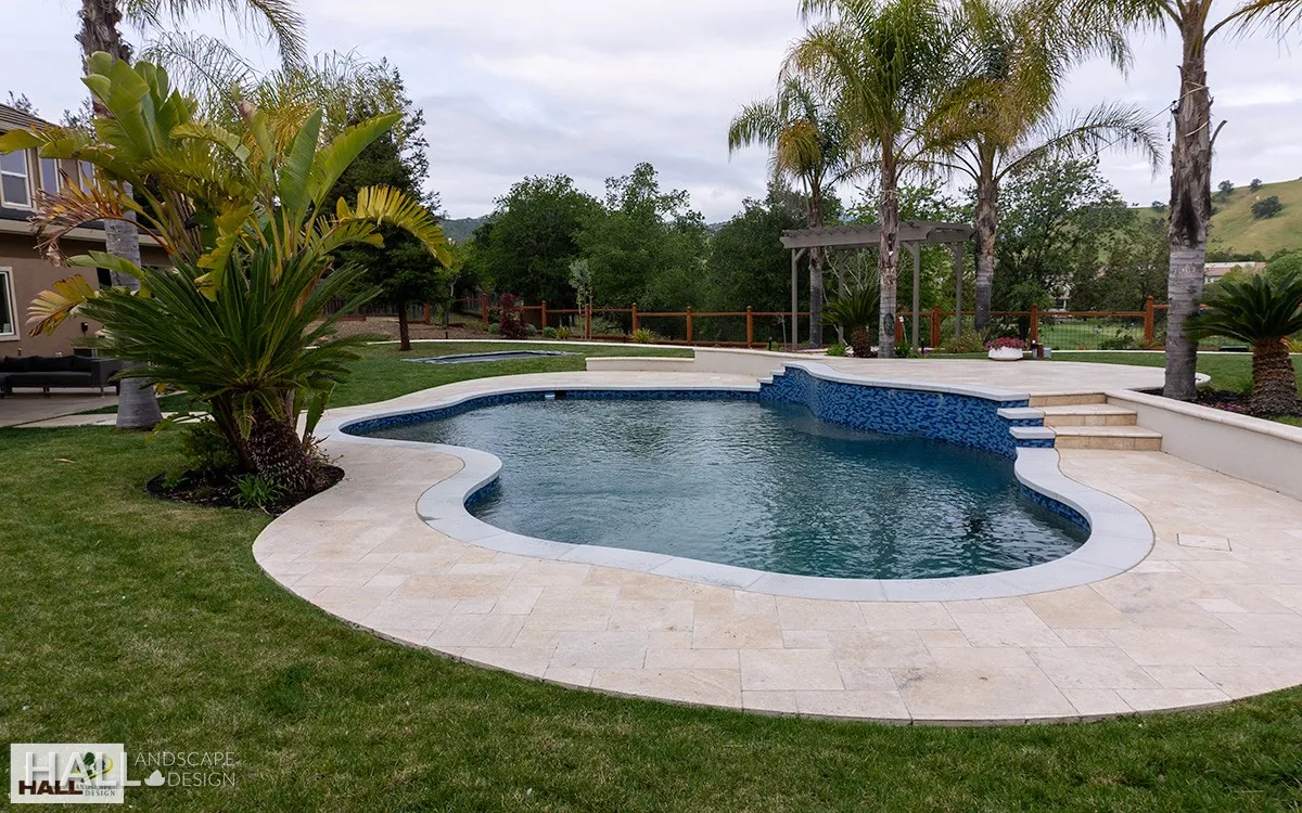 After — Fenced-off pool in a bare lawn → resort pool & travertine deck in Fairfield