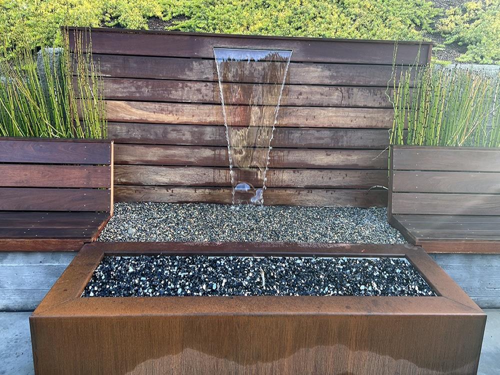 Water feature built into side of hill with snake grass growing in planters on either side. 