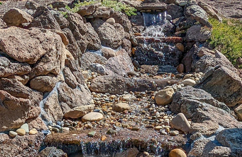 Water feature designed to look like a natural, small waterfall spilling down a rocky hillside. 